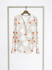 A long-sleeve button-up blouse with a white base and an orange and white abstract pattern, hanging on a wooden hanger from a minimalist gray clothing display stand against a white studio background.