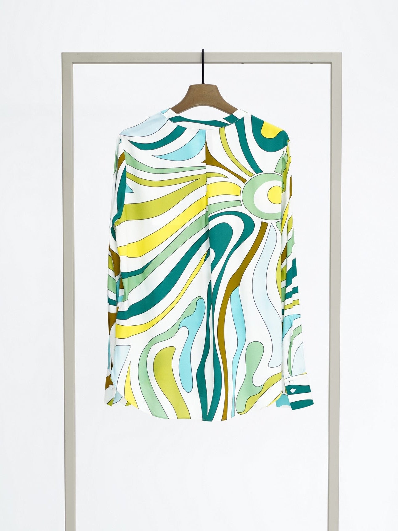 A long-sleeve button-up shirt with a colorful abstract wavy pattern in teal, yellow, green, and white, hanging on a wooden hanger from a minimalist silver clothing rack against a white background.
