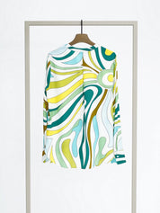 A long-sleeve button-up shirt with a colorful abstract wavy pattern in teal, yellow, green, and white, hanging on a wooden hanger from a minimalist silver clothing rack against a white background.