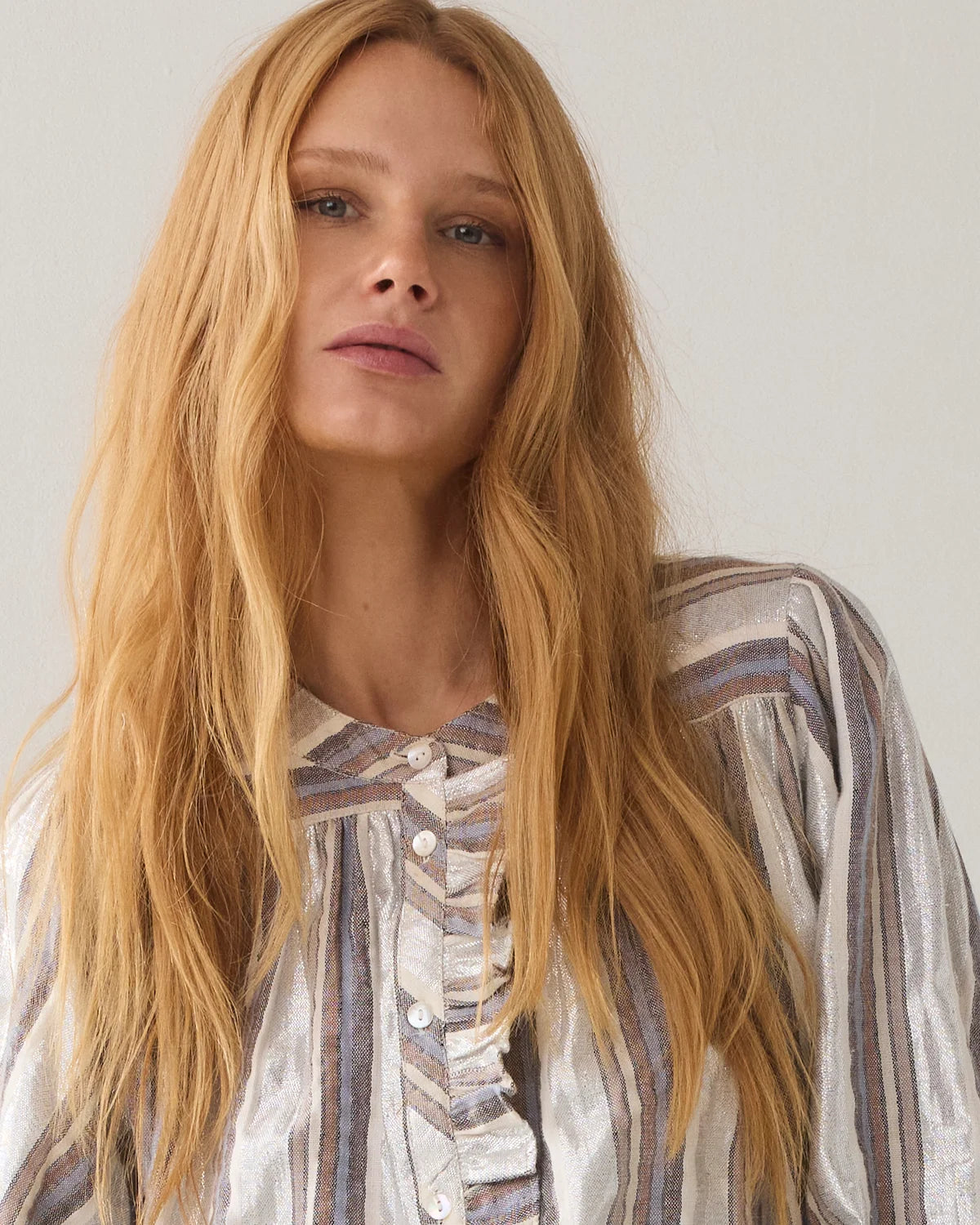 Woman with long blonde hair wearing a striped shirt against a plain background