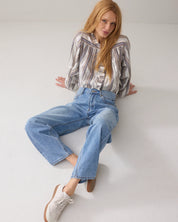 Woman wearing a striped shirt and blue jeans sitting on a white floor.
