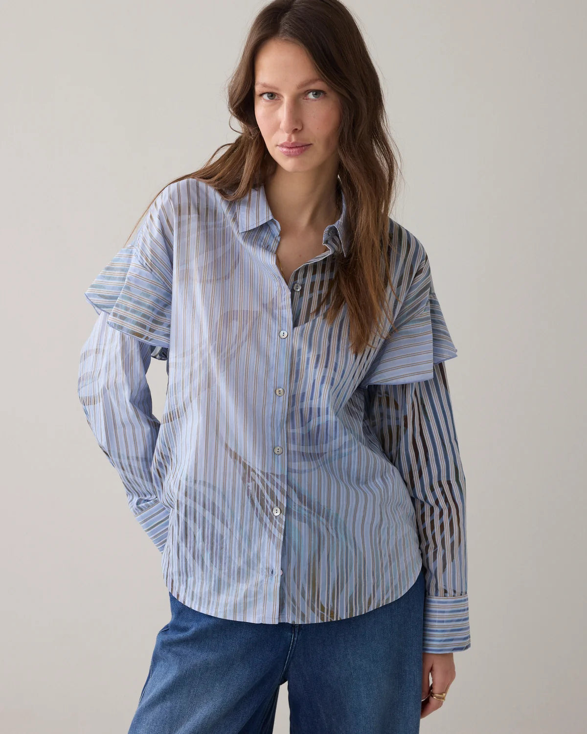 Woman wearing a striped shirt and blue pants against a plain background