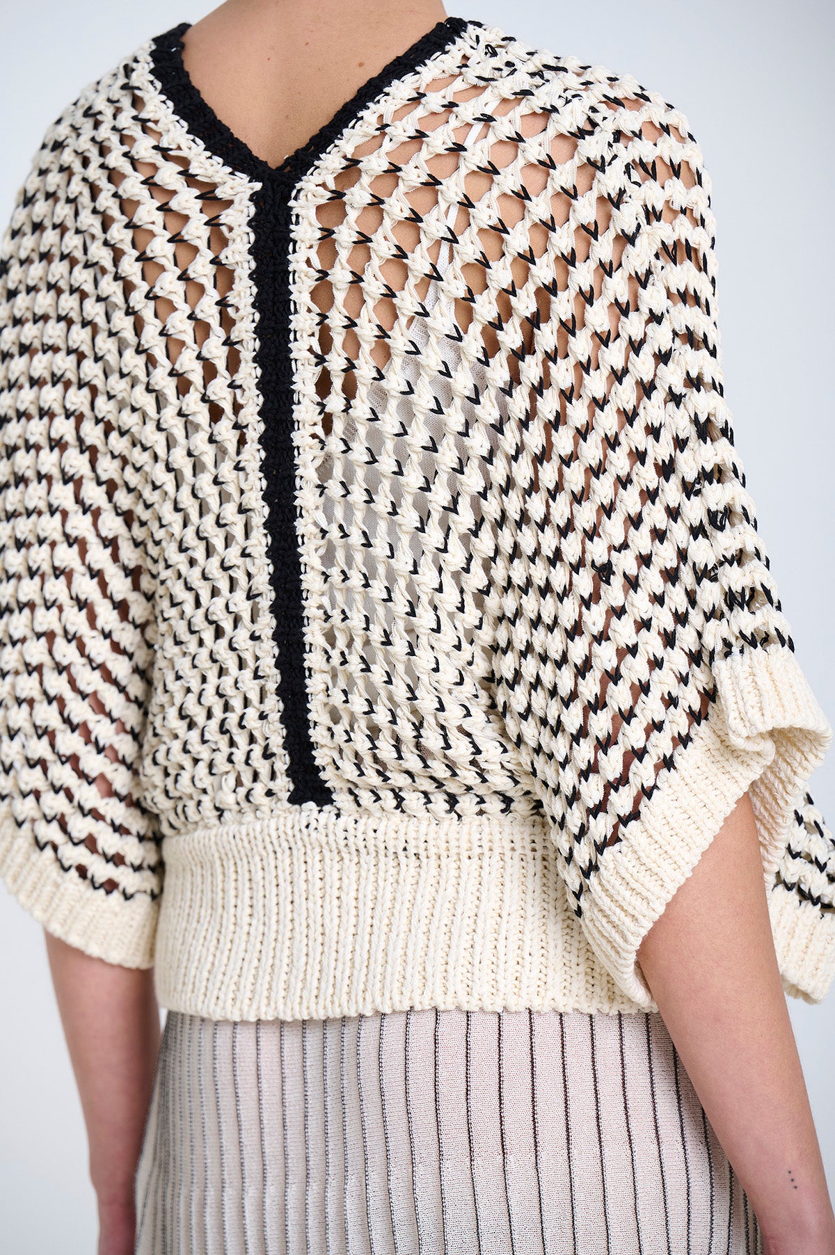 Knitted sweater with an open weave in ecru and black geometric pattern on a plain background