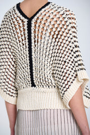 Knitted sweater with an open weave in ecru and black geometric pattern on a plain background