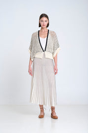 Woman wearing a open weave cardigan cardigan over a radial skirt on a white background