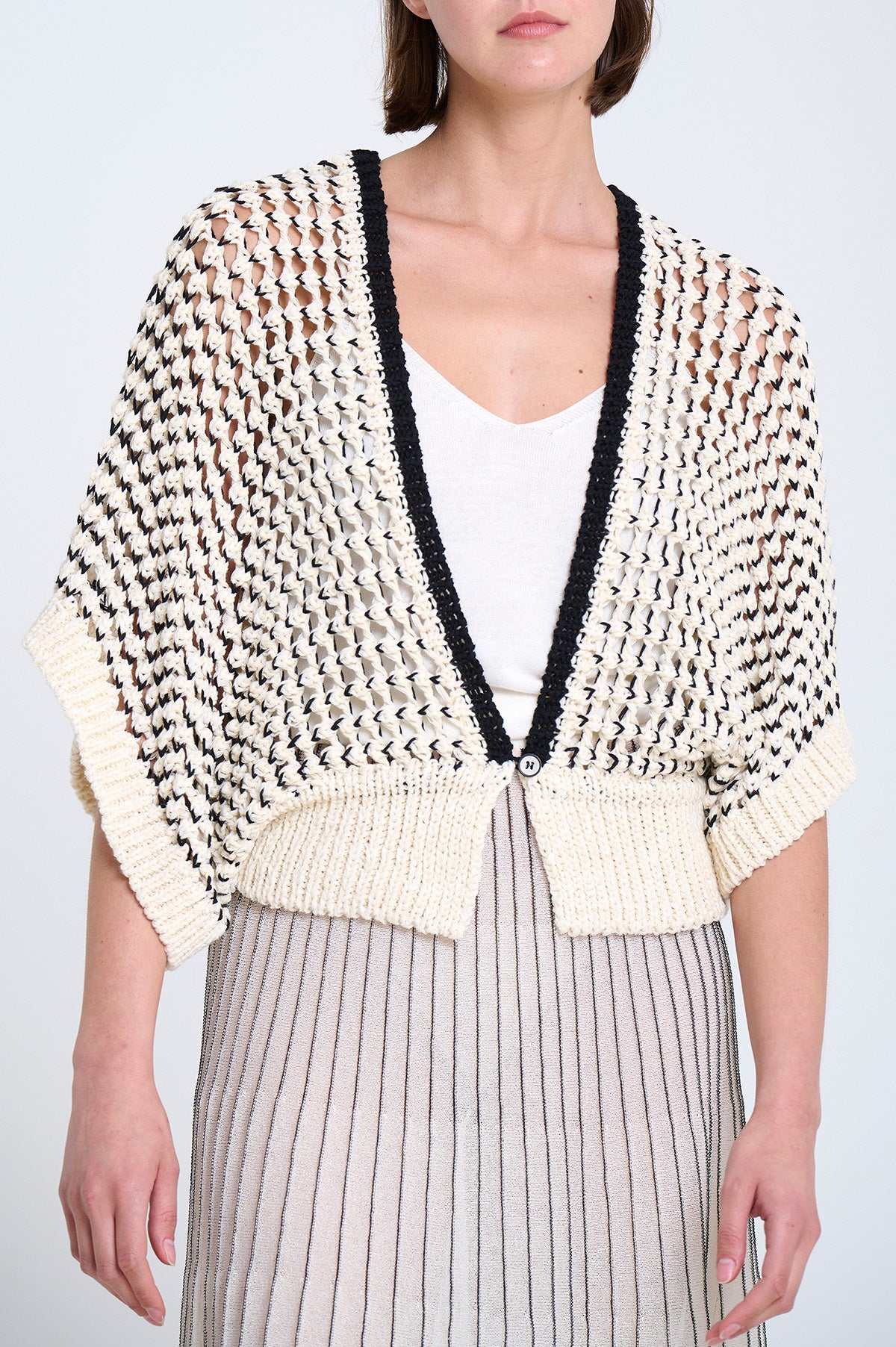 Woman wearing a patterned cardigan over a white top and striped skirt on a light background