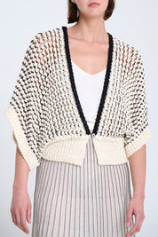 Woman wearing a patterned cardigan over a white top and striped skirt on a light background