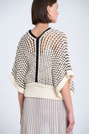 Woman wearing a beige and black patterned top with a plain background