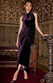 Woman standing in a room with textured wallpaper wearing Sacha Drake Lavish Velvet Cowl Dress in Amethyst 