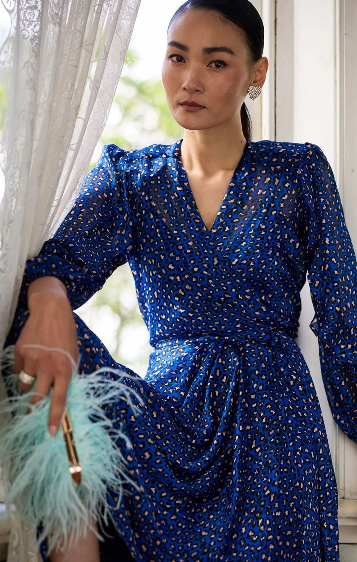 Woman wearing a blue wrap dress with patterns indoors.