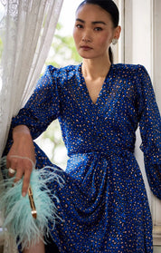 Woman wearing a blue wrap dress with patterns indoors.